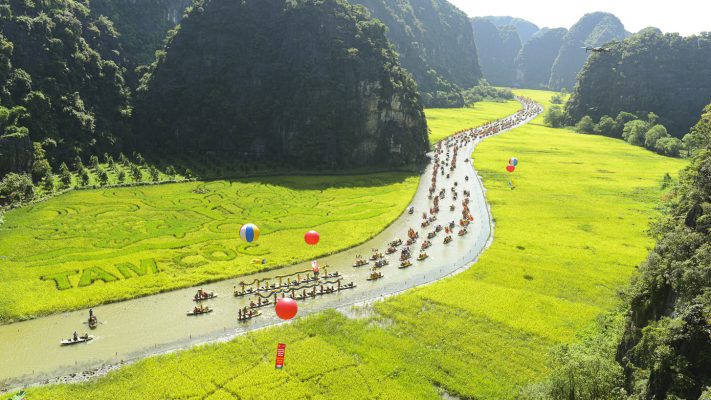 Sampan boat navigating through the three caves of Tam Coc, Ninh Binh - A scenic landscape of rice fields and karst mountains.